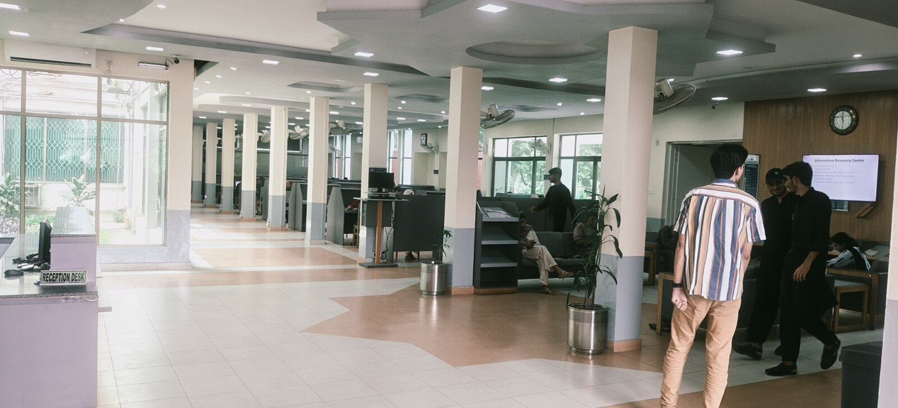 Library reception and lounge with seating, indoor plants, and visitors
